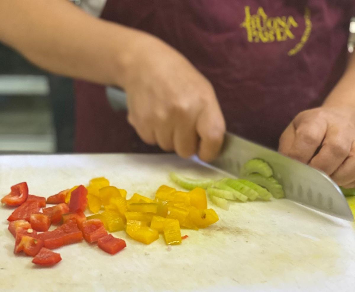 Chef con delantal de La Buona Pasta cortando pimientos frescos en la cocina