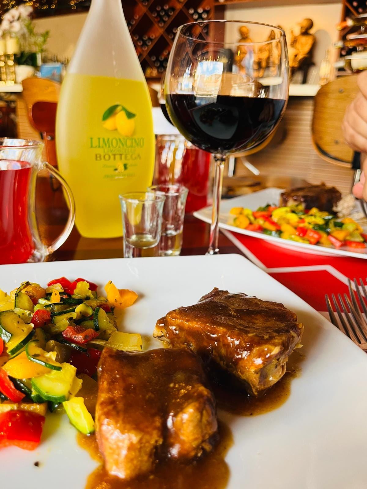 Carne jugosa con vegetales asados acompañada de vino tinto y limoncino