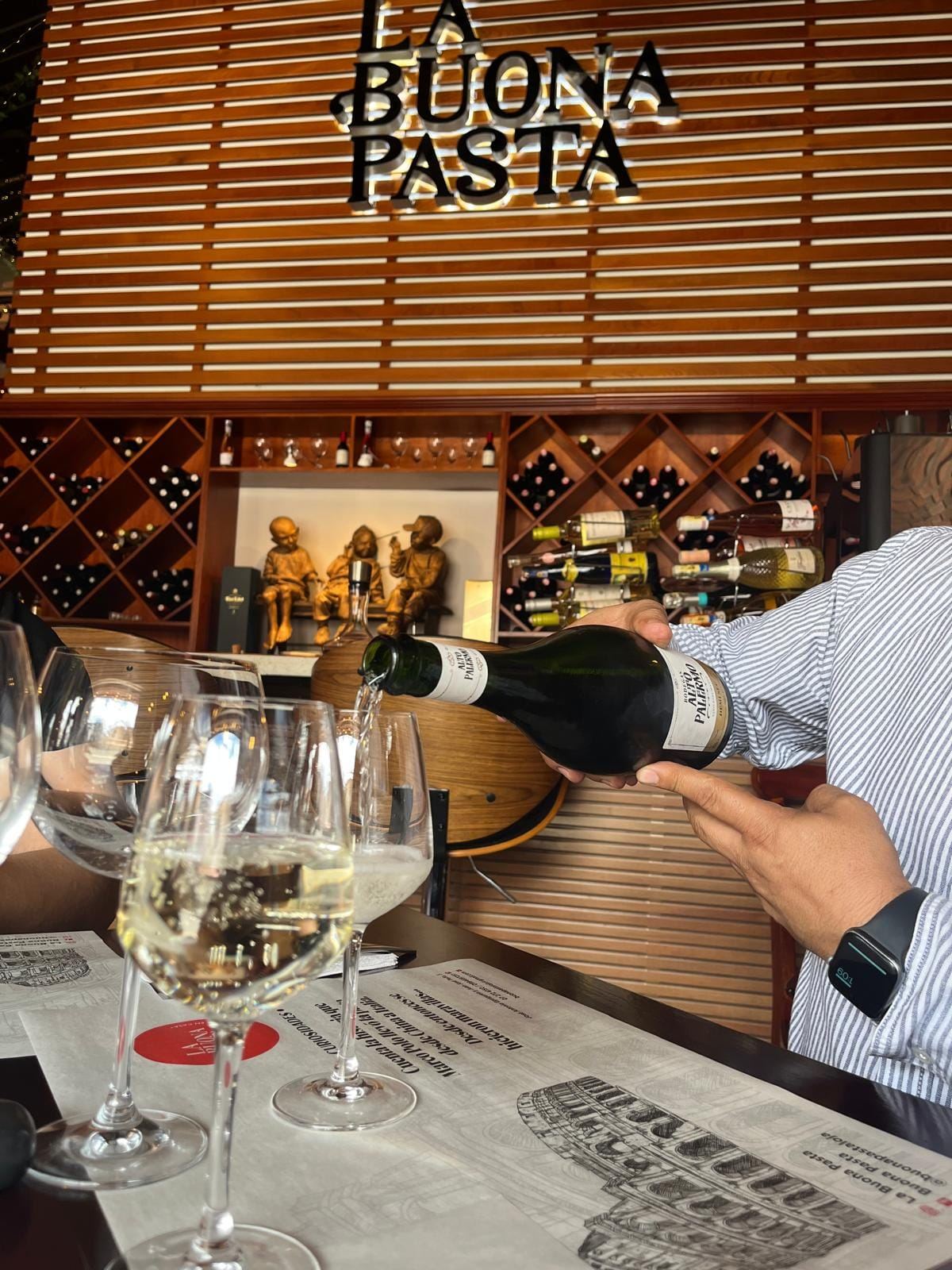 Sirviendo vino blanco con letrero dorado de La Buona Pasta y bodega de vinos